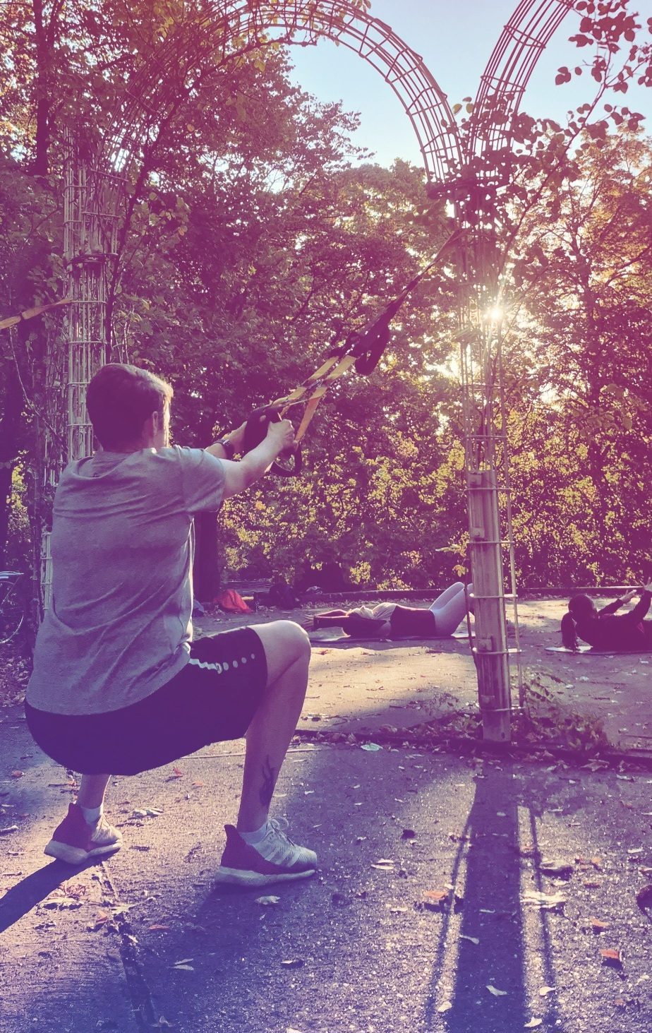 Schlingentraining (TRX) an der Pergola, im Hintergrund Bauchübungen auf der Matte – Sport im Park in Berlin